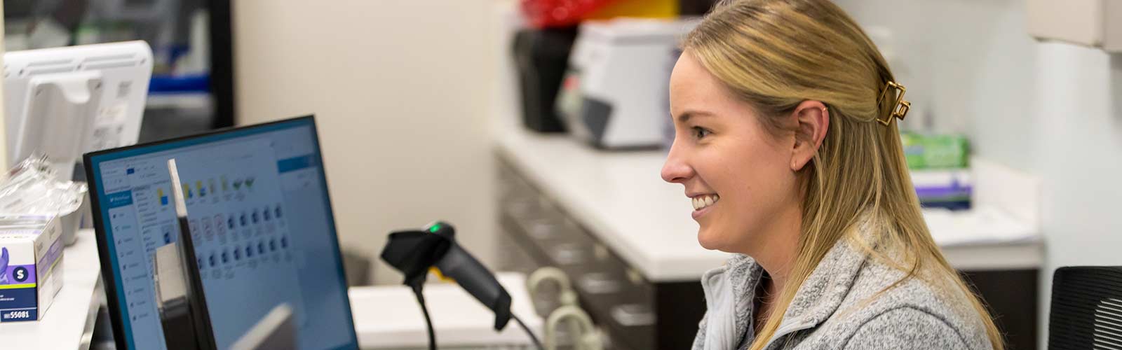 A woman smiles as she sits behind a desk at a medical office